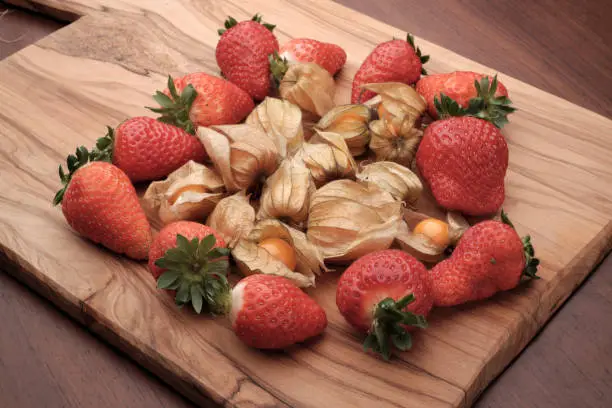 Physalis fruit on a cutting board, together with straberries