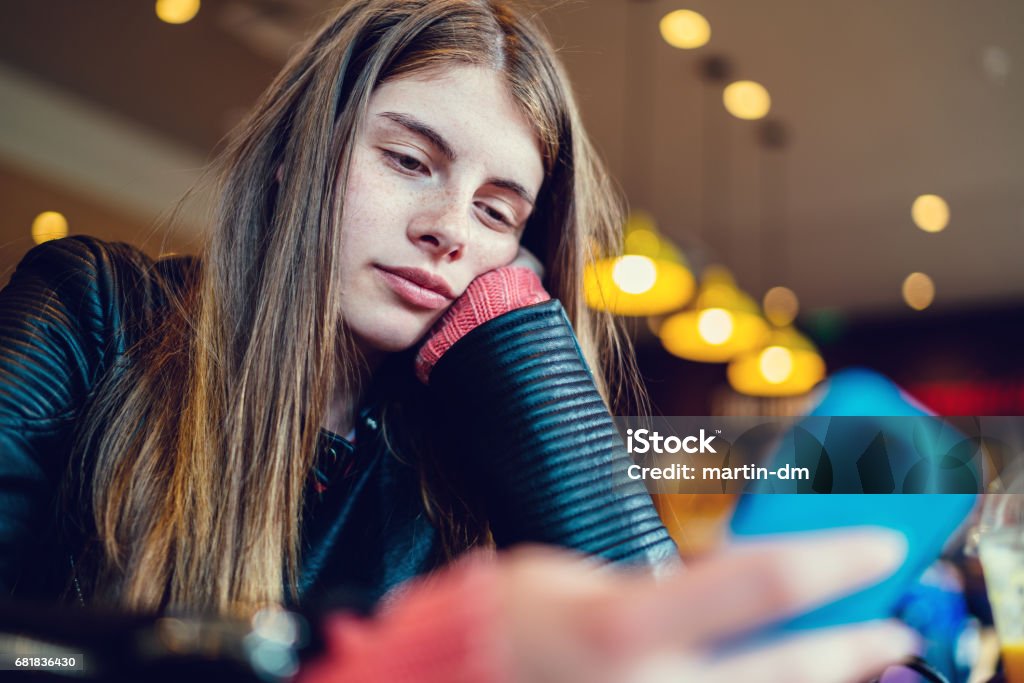 Bored girl in cafe texting Teenage girl in cafe text messaging on smartphone Teenager Stock Photo