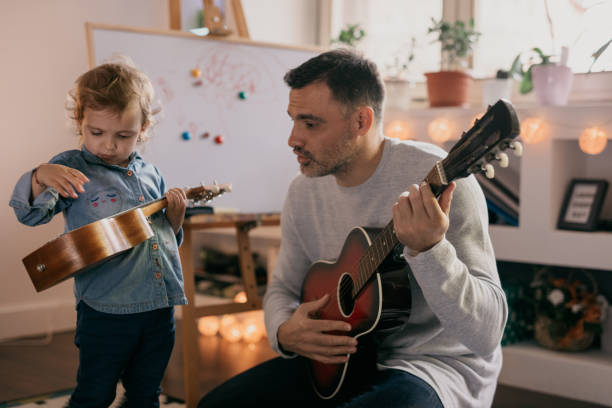 istock Child having fun with ukulele while her father is playing a guitar 681849152