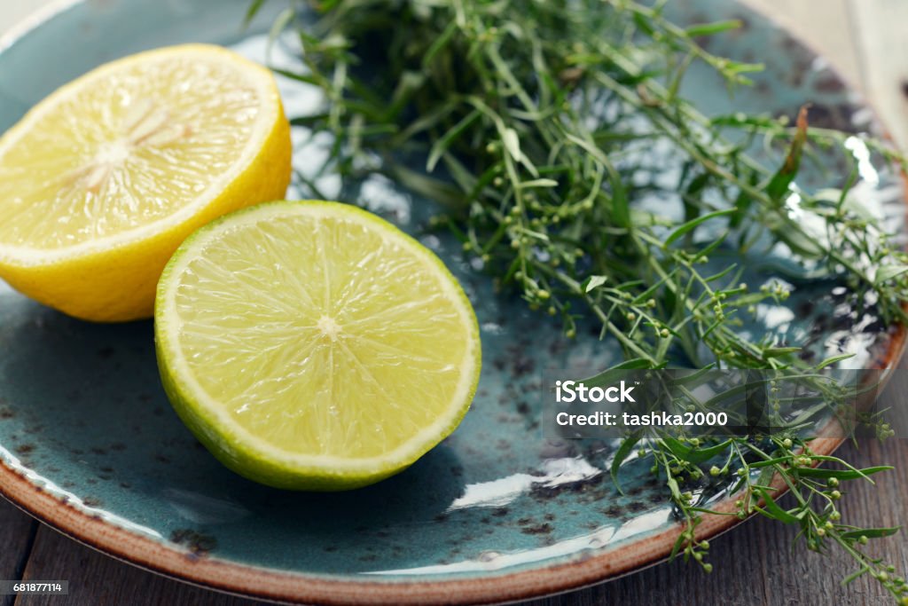 Tarragon with lemon and lime Fresh tarragon with lemon and lime on plate on wooden background Bunch Stock Photo