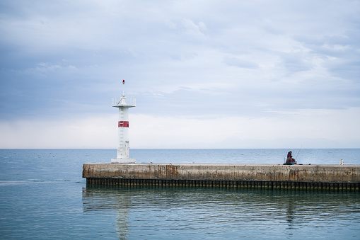 Manavgat harbour entrance and lighthouse with man fishing, bad weather