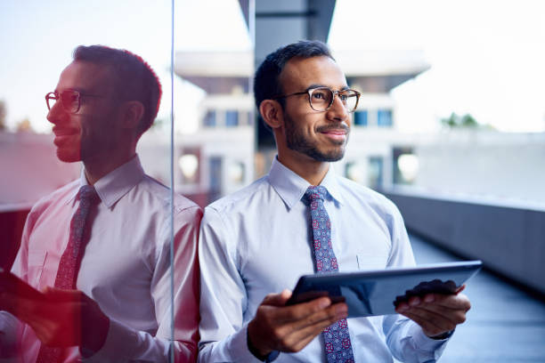 millenial businessman leaning confidently on a dark glass wall with cityscape background - povo indiano imagens e fotografias de stock