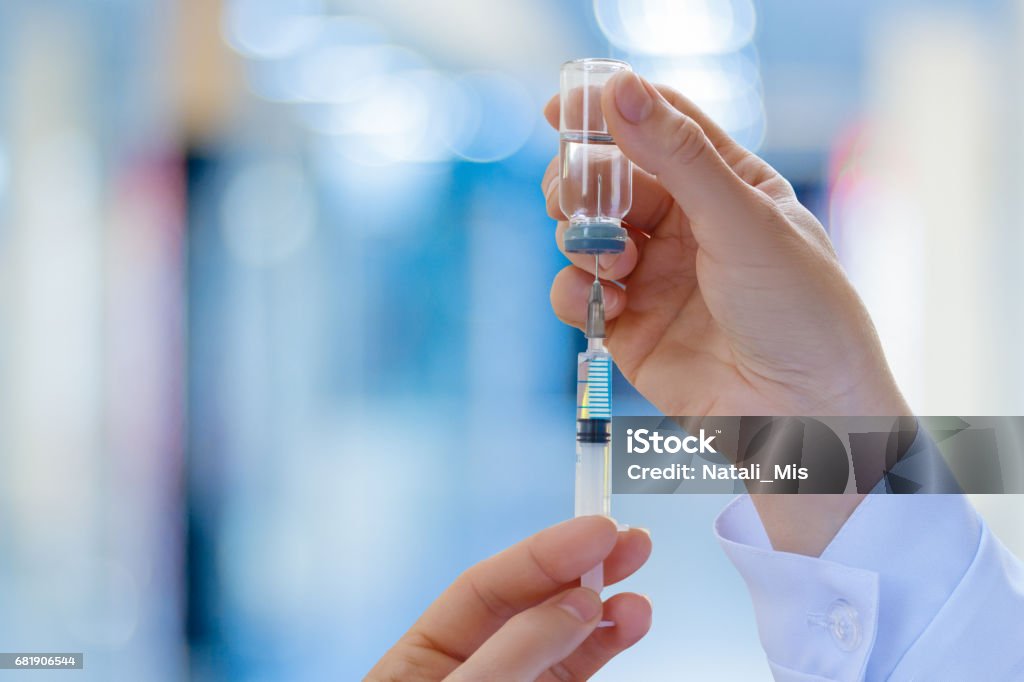 The doctor fills a syringe with vaccine . The doctor fills a syringe with vaccine on blurred background. Injecting Stock Photo