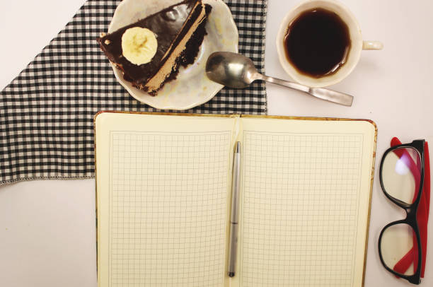 A journalist's breakfast, a writer's lunch, a sweet tooth dinner. On the photo: a notebook, a pen, a chocolate cake, a cup of tea and reading glasses. Objects isolated on white background