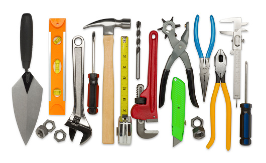This is an overhead photo of construction tools isolated on white background. There is a level, nuts, ranch, screwdriver, hammer, tape measure, drillbit, plumber's wrench, rivet hole puncher, razor blade, pliers, measuring tool, and more.