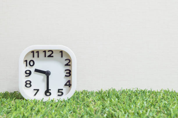 istock Closeup white clock for decorate show a half past nine or 9:30 a.m. on green artificial grass floor and cream wallpaper textured background with copy space 682060572