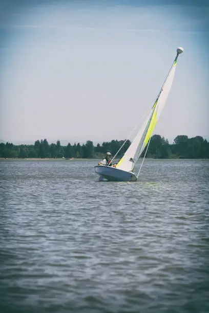 A teenage boy in a very small sailboat on a lake learns to manage the craft as it tilts in strong winds