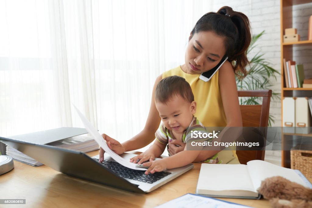 Working mother Young woman working with baby on her knees Working Mother Stock Photo