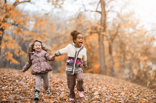 Cute friends holding hands and having fun while running in the forest.