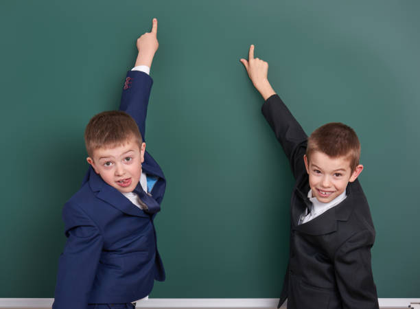 istock school boy point finger at blank chalkboard background, dressed in classic black suit, group pupil, education concept 682125746