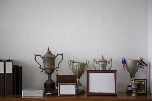 Old silver trophies, picture frames and file folders on a sideboard cabinet in an retro style office.