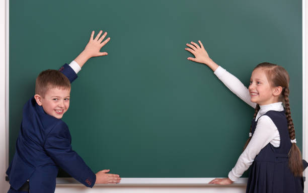 istock elementary school boy and girl put hands on chalkboard background and show blank space, dressed in classic black suit, group pupil, education concept 682126332