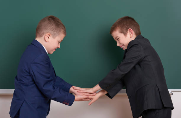 istock two friends handshake, elementary school boy near blank chalkboard background, dressed in classic black suit, group pupil, education concept 682126404
