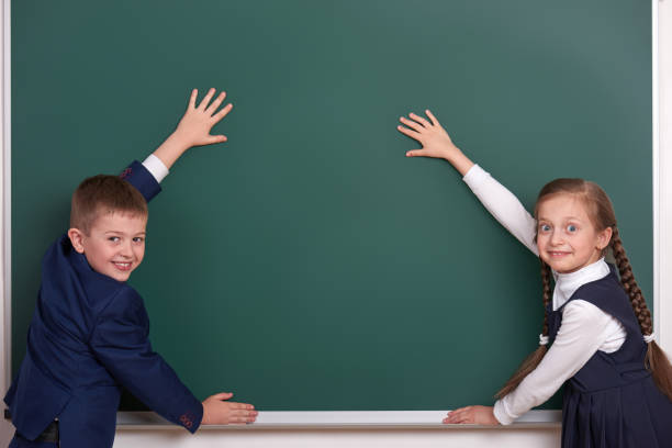 istock elementary school boy and girl put hands on chalkboard background and show blank space, dressed in classic black suit, group pupil, education concept 682126444