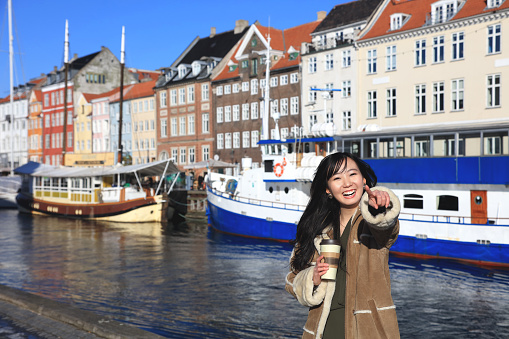 Happy japanese woman tourist sightseeing in popular tourist area, Nyhavn, Copenhagen, Denmark. - February 15, 2017