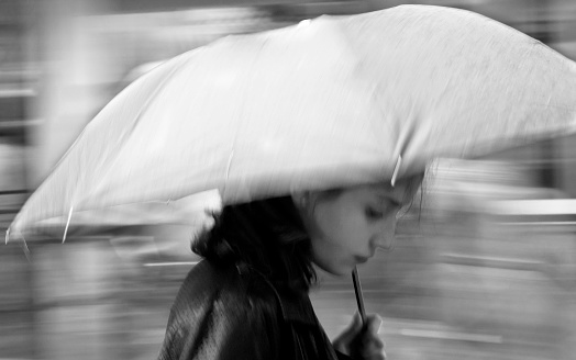 Belgrade, Serbia: Blurry young woman under umbrella walking on the city street on a rainy spring day,  in black and white