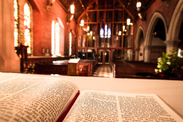 Open bible on the altar inside an English Anglican church Close up image of the Holy Bible open at the book of John on the altar of an Anglican church. The pews and stained glass windows of the interior of the church are blurred out of focus in the background, and warm orange sunlight is streaming in through the windows. Horizontal colour image with copy space. anglican eucharist stock pictures, royalty-free photos & images