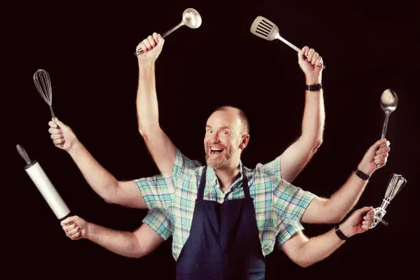 A smiling mature man with six arms - in the style of a Hindu deity - multitasks with various kitchen utensils against a black background