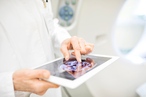 Midsection of female doctor examining X-ray image in digital tablet. Close-up of surgeon is analyzing reports in examination room. She is standing in hospital.