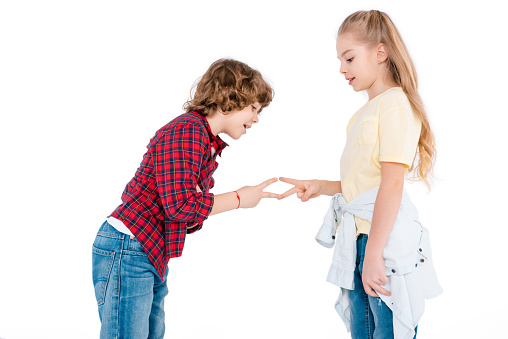 Cute boy and girl playing in rock-paper-scissors game isolated on white