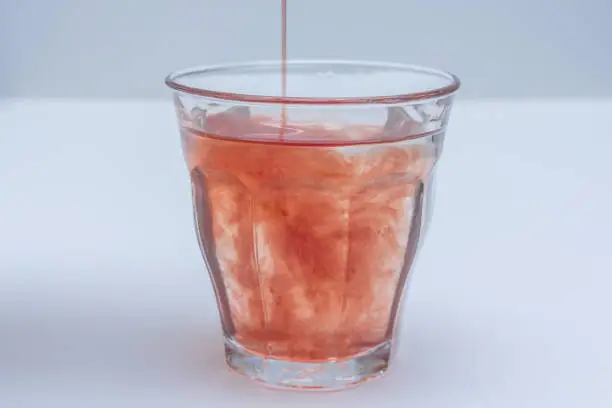 fruit juice extract poured into glass of water on white background