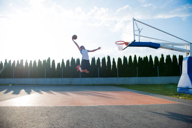 Young man jumping and making a fantastic slam dunk playing streetball, basketball. Urban authentic.