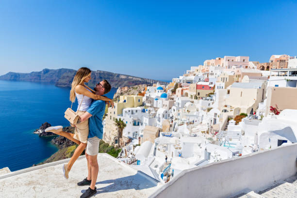 Young couple on island of Santorini Young couple looks down on the landscape of the island of Santorini happy couple on vacation in santorini greece stock pictures, royalty-free photos & images