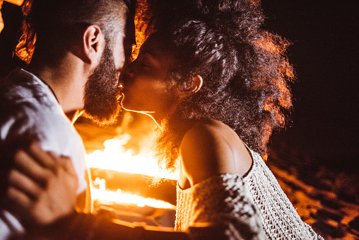 Couple kissing at the beach next to fireplace.