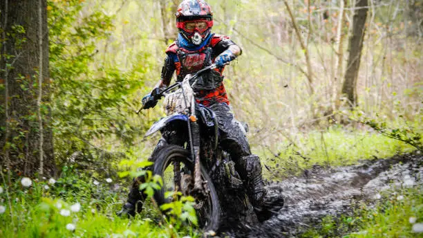 An 11 year-old boy riding his dirt bike through a muddy trail in the forest.