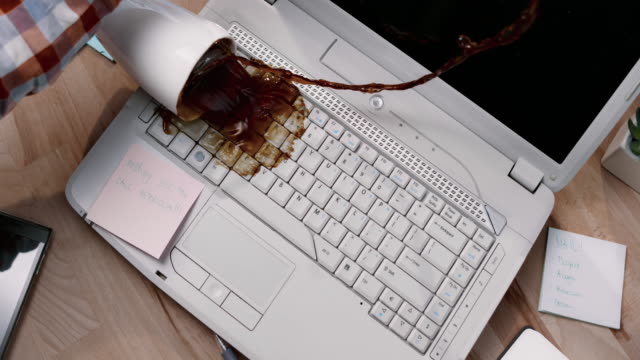 SLO MO LD Man knocking over a cup of coffee which spills all over his white laptop