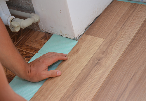 Man Installing Laminate Wood Flooring in Problem Area. Worker Installing wooden laminate flooring. Handyman laying down laminate flooring boards while renovating a house.