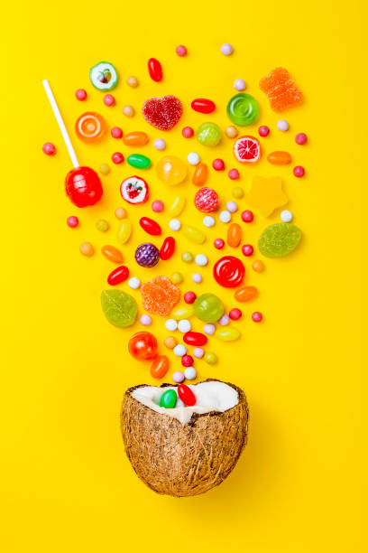 Colorful explosion of candies in coconut on yellow colored background, creative still life, flat lay style