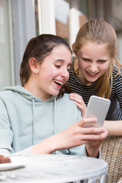 istock Two Young Girls At Cafe Reading Text Message On Mobile Phone 682236004