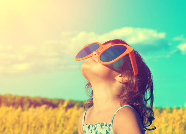 Happy little girl with big sunglasses looking at the sun in the wheat field in summer Happy little girl with big sunglasses looking at the sun in the wheat field in summer mesmerised stock pictures, royalty-free photos & images