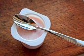 pink yogurt in plastic cup on wooden background with spoon.