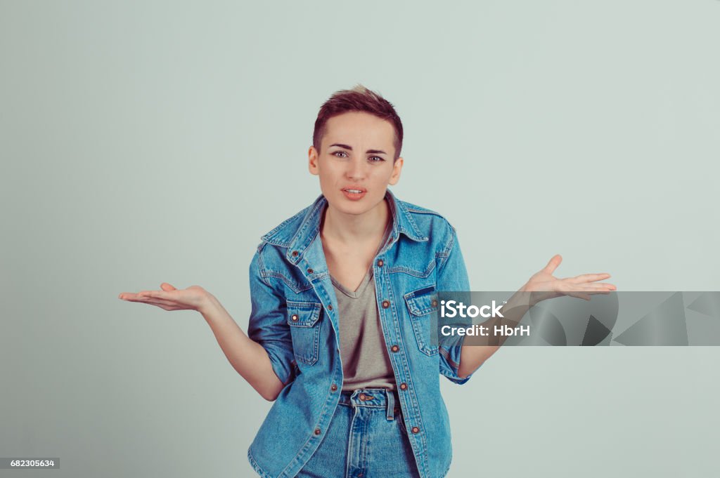 Closeup portrait puzzled clueless young woman with arms out asking what is problem who cares so what I don"u2019t know isolated grey background. Negative human emotion face expression reaction perception Shrugging Stock Photo