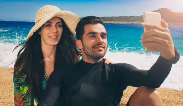 Young couple taking selfies with their mobile phone on the beach.
