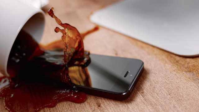 SLO MO LD Coffee cup spilling all over a black mobile phone on the table