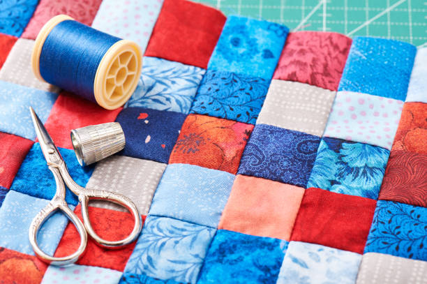 scissors, thread and thimble lying on blue and red square pieces of fabric sewn together - quilt textile patchwork thread imagens e fotografias de stock