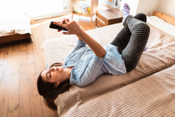 adolescente fare un selfie sul letto - one teenage girl only on the phone bed lying on front foto e immagini stock