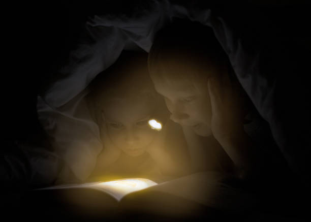 istock Sister and brother are reading a book under a blanket with flashlight. 682366540