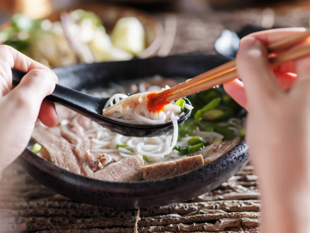 istock woman eating pho with sriracha using chopsticks and spoon together 682377586