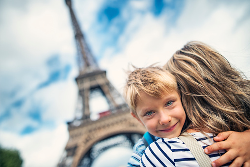 Mother and little boy visiting Paris. They are embracing in front of the Eiffel Tower. Happy little boy is looking over the mum's shouder into the camera. The boy is aged 5.
