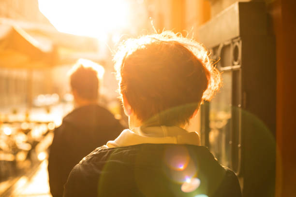 An adult woman walks down the street towards the sun