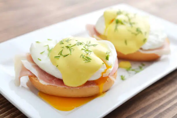Classic Egg Benedict on white plate on wooden background