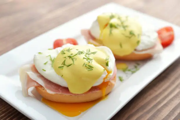 Classic Egg Benedict on white plate on wooden background