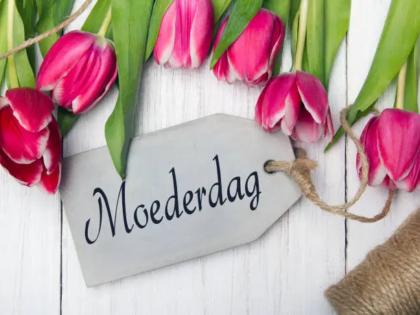 Photo of Mother's day card  with Dutch words: Mother's day. Tulip bouquet on white wooden background, copy space