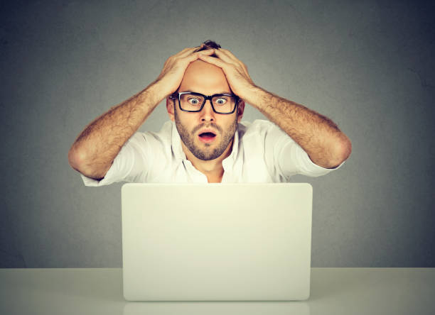 istock Shocked young man looking at laptop computer anxious with open mouth 682419662