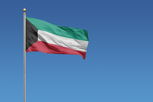 Flag of Kuwait in front of a clear blue sky