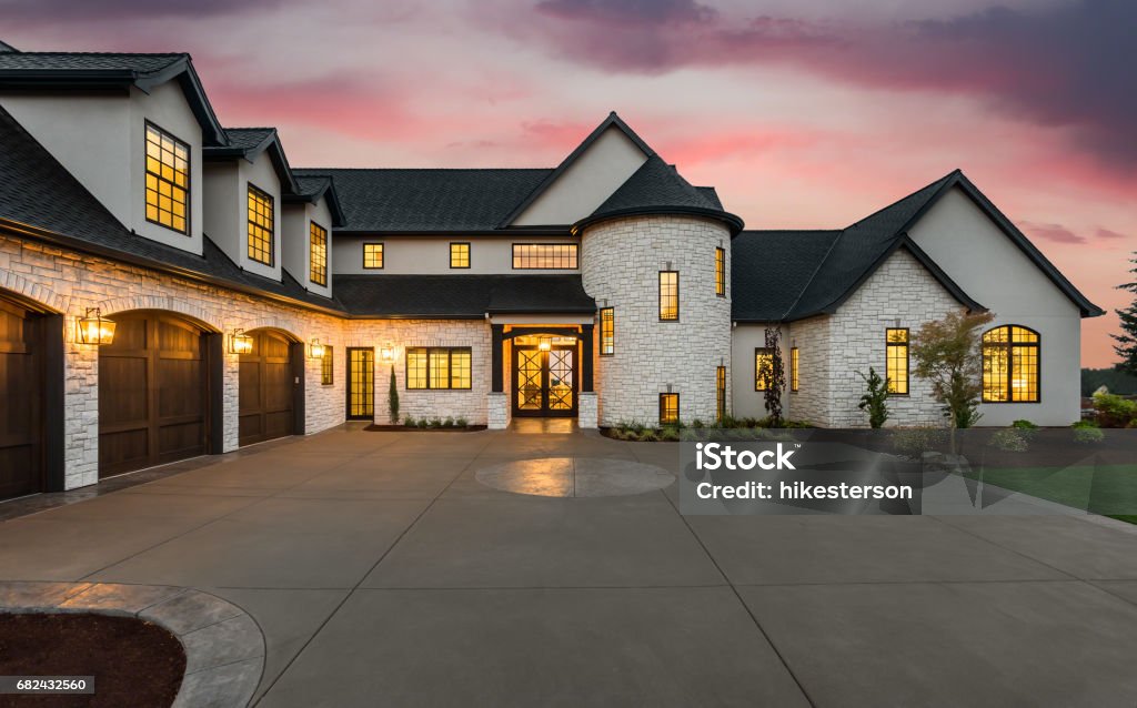 Stunning luxury home exterior at sunset new luxury home with three car garage, large driveway and glowing exterior and interior lights Luxury Stock Photo